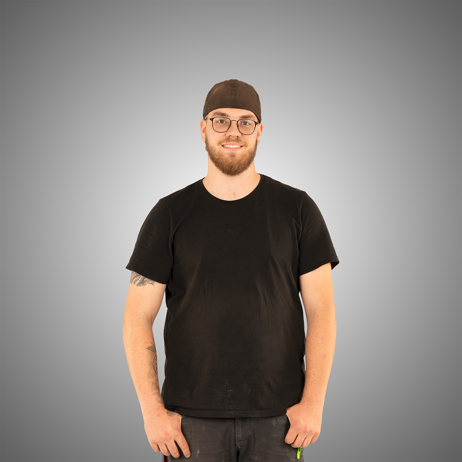 Laechelnder Mann mit Brille Bart brauner Muetze und schwarzem T Shirt