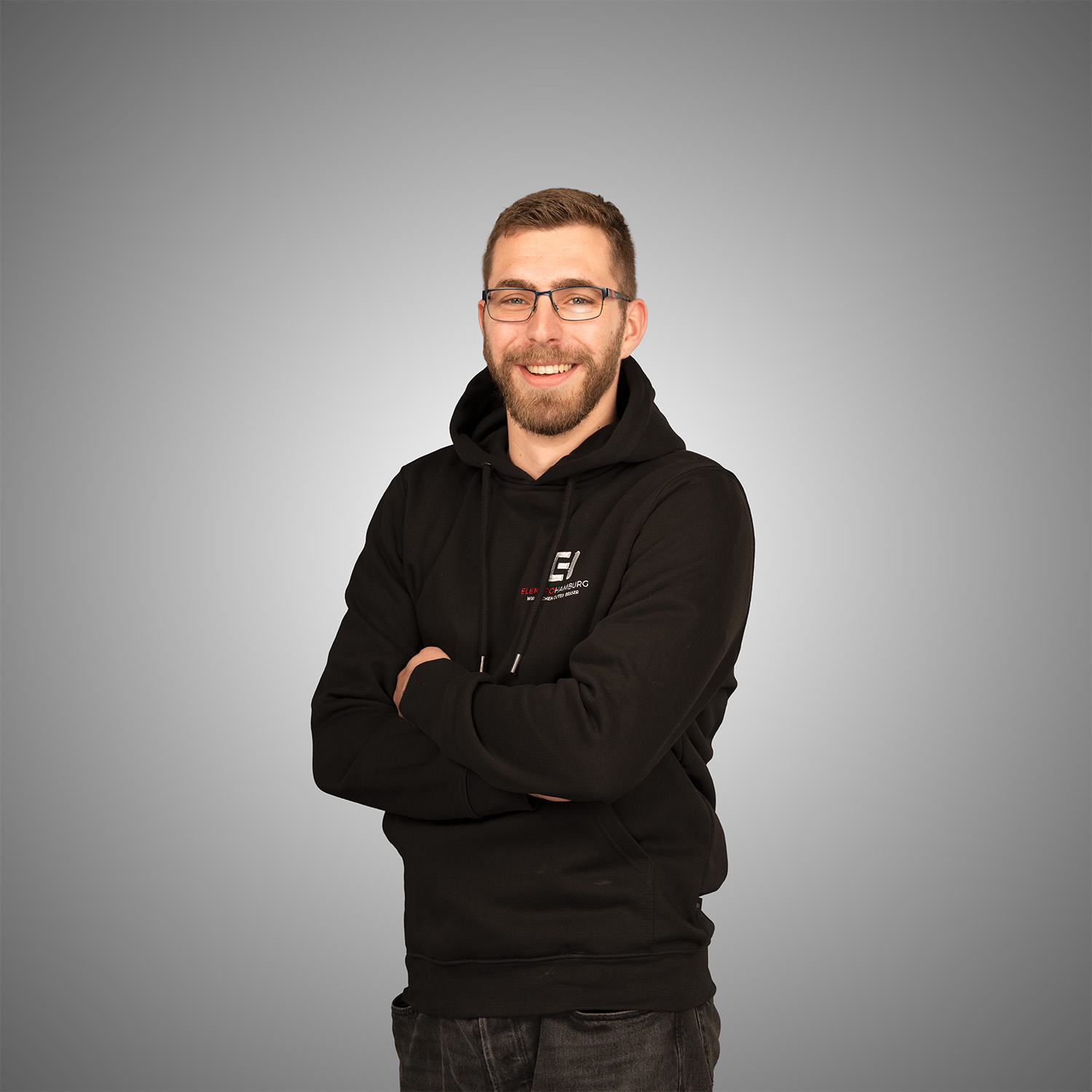 Laechelnder Mann mit Brille und Bart im schwarzen Hoodie mit Firmenlogo