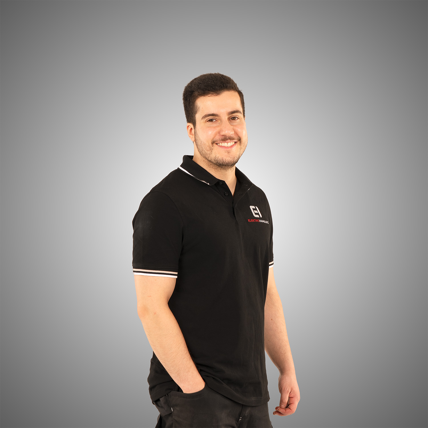 Laechelnder junger Mann mit dunklem Haar im schwarzen Poloshirt mit Firmenlogo