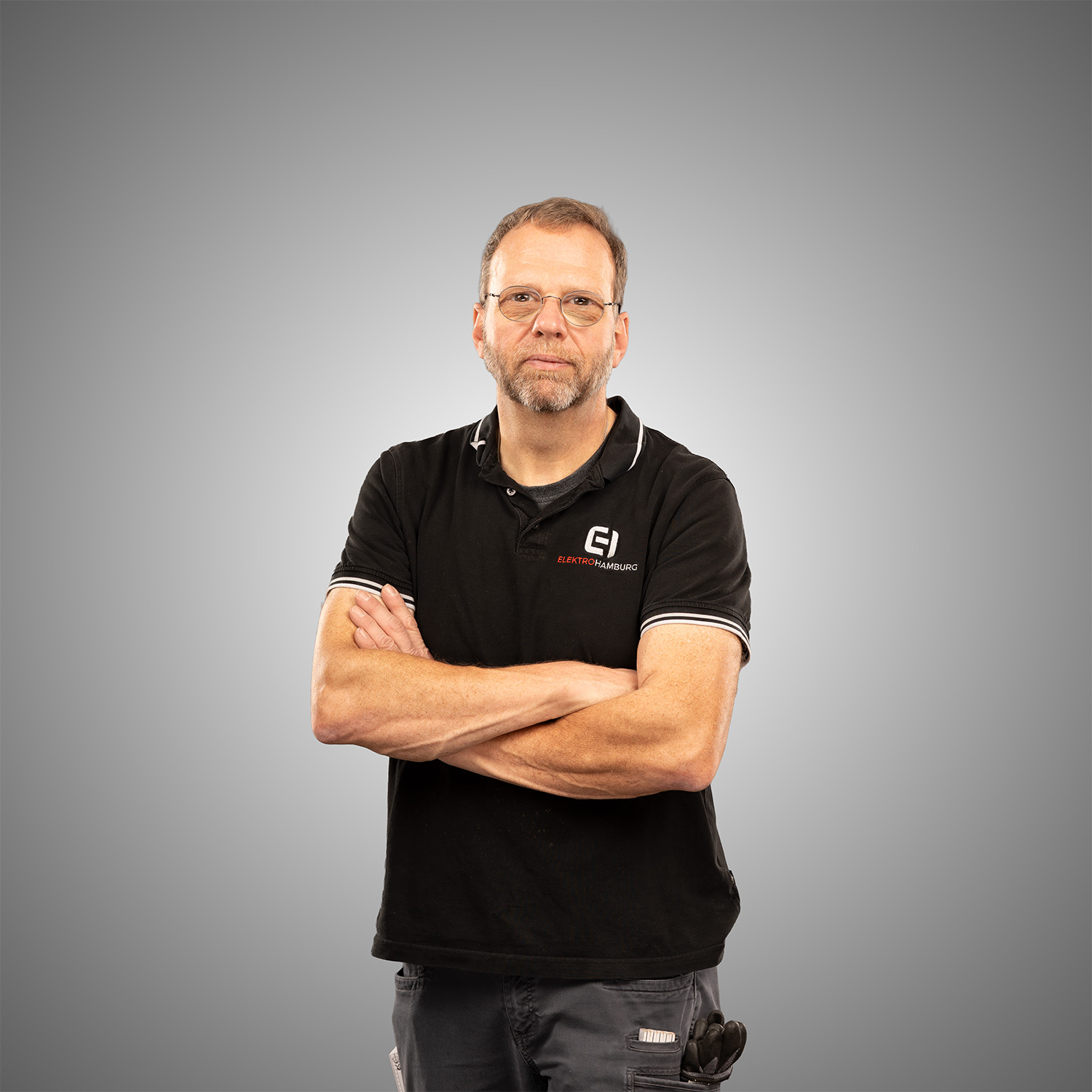 Mann mit Brille und Bart im schwarzen Elektro Hamburg Poloshirt mit verschraenkten Armen