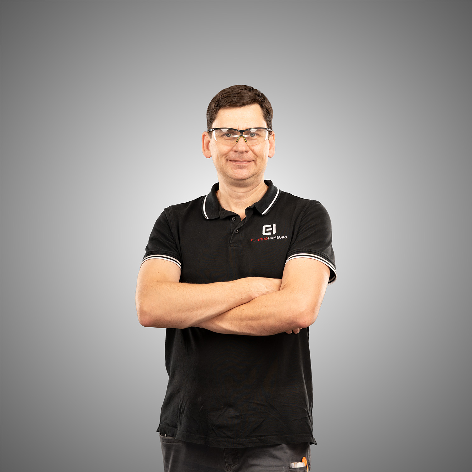 Laechelnder Mann mit Schutzbrille im schwarzen Elektro Hamburg Poloshirt