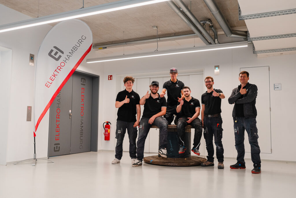 Sechs laechelnde Elektro Hamburg Mitarbeiter in schwarzer Kleidung mit Daumen hoch