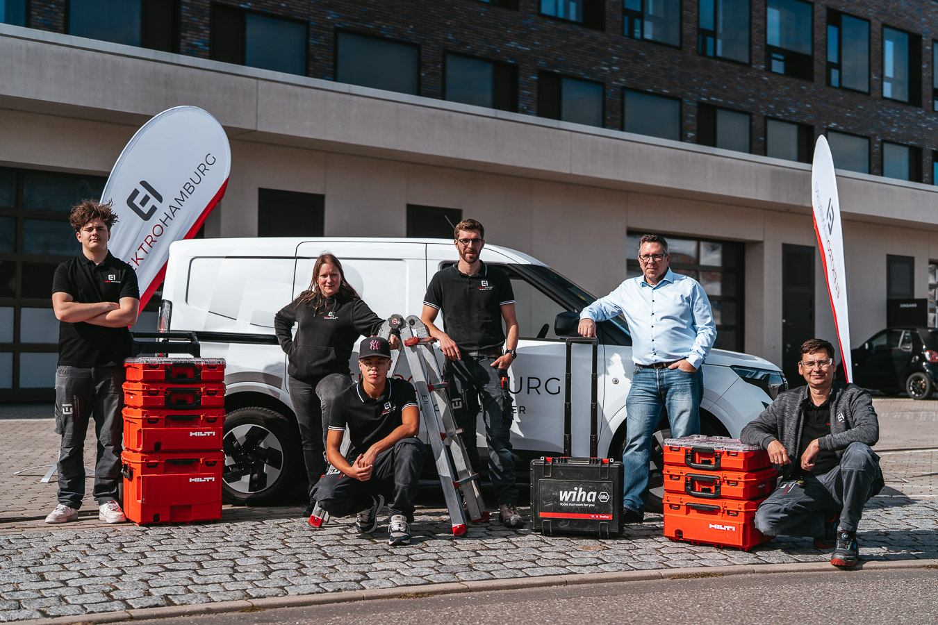 Sechskoepfiges Elektriker Team posiert selbstbewusst vor weissem Firmenwagen